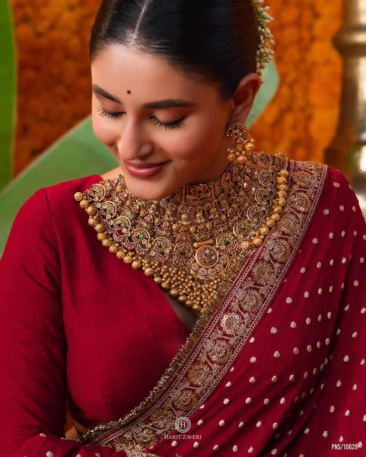A woman in a red saree wearing a gold choker and jhumkas