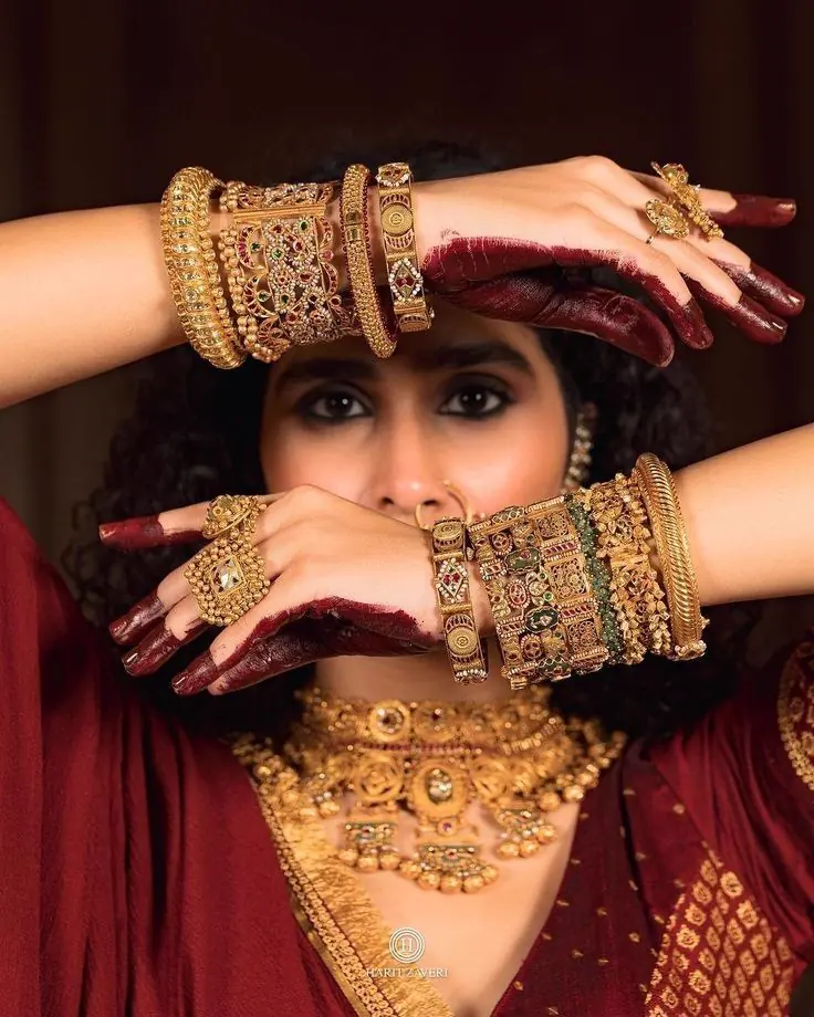 Hands with mehendi wearing stacked gold bangles and rings