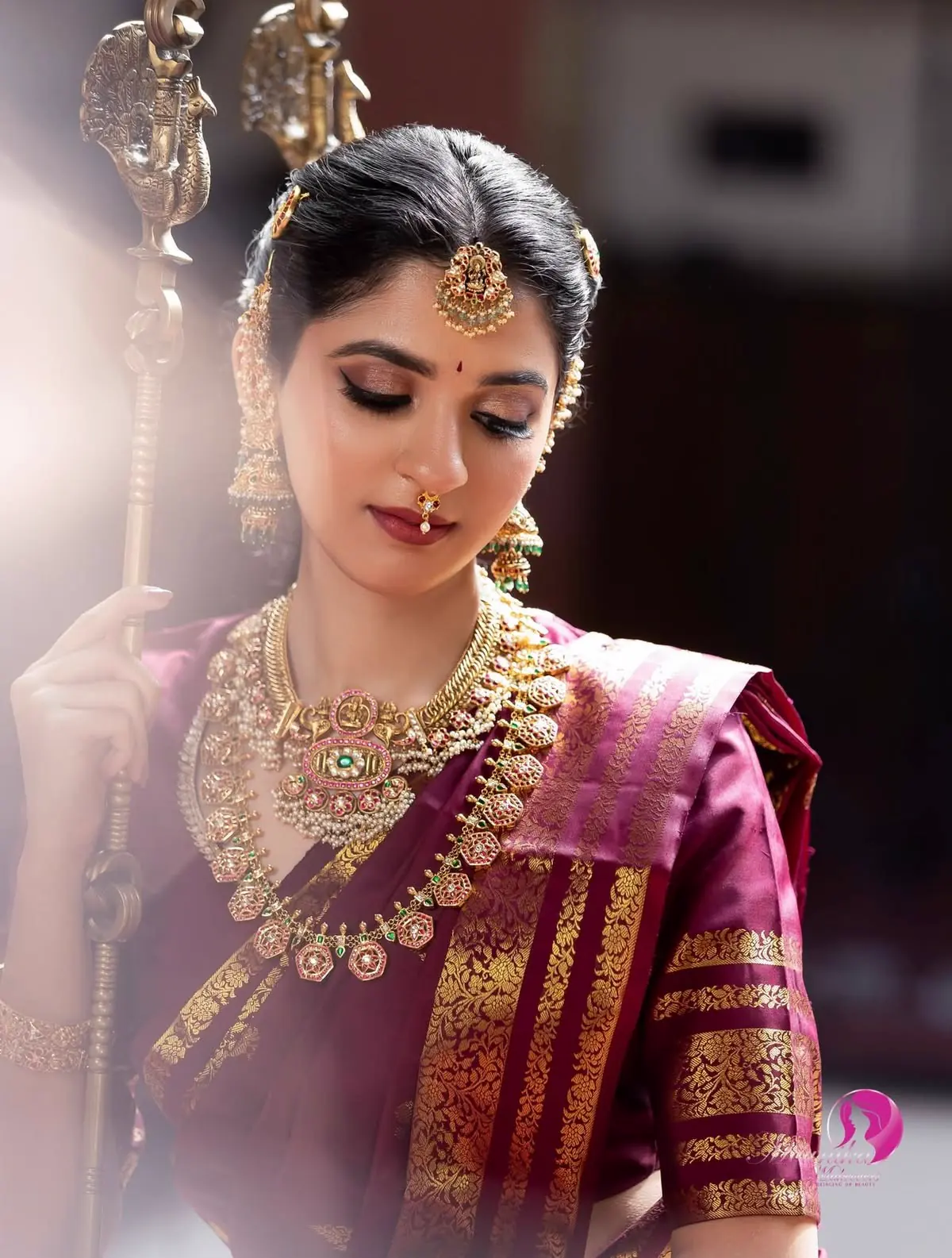 A bride in a magenta silk saree wearing a layered temple necklace