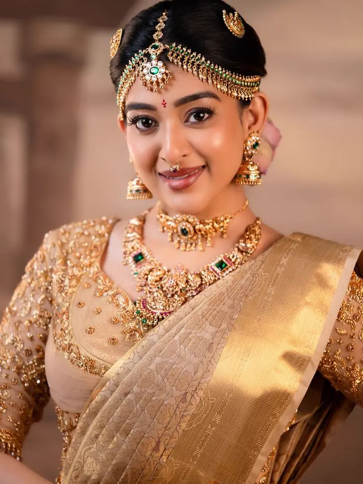 A bride wearing a gold and emerald necklace set with matching earrings